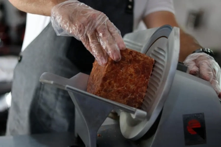 A man cutting meat on a slicer